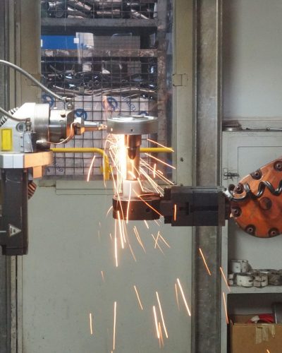 A robotic arm welding in an industrial setting, emitting bright sparks.