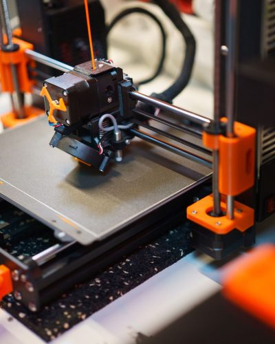 Detailed view of a 3D printer creating an object with orange components.
