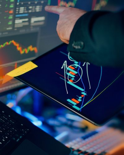 A business professional examines financial charts on a tablet and monitor for investment strategy.