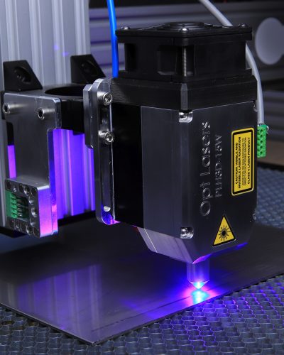 Close-up of a laser engraving machine operating on a metal surface with blue laser light.